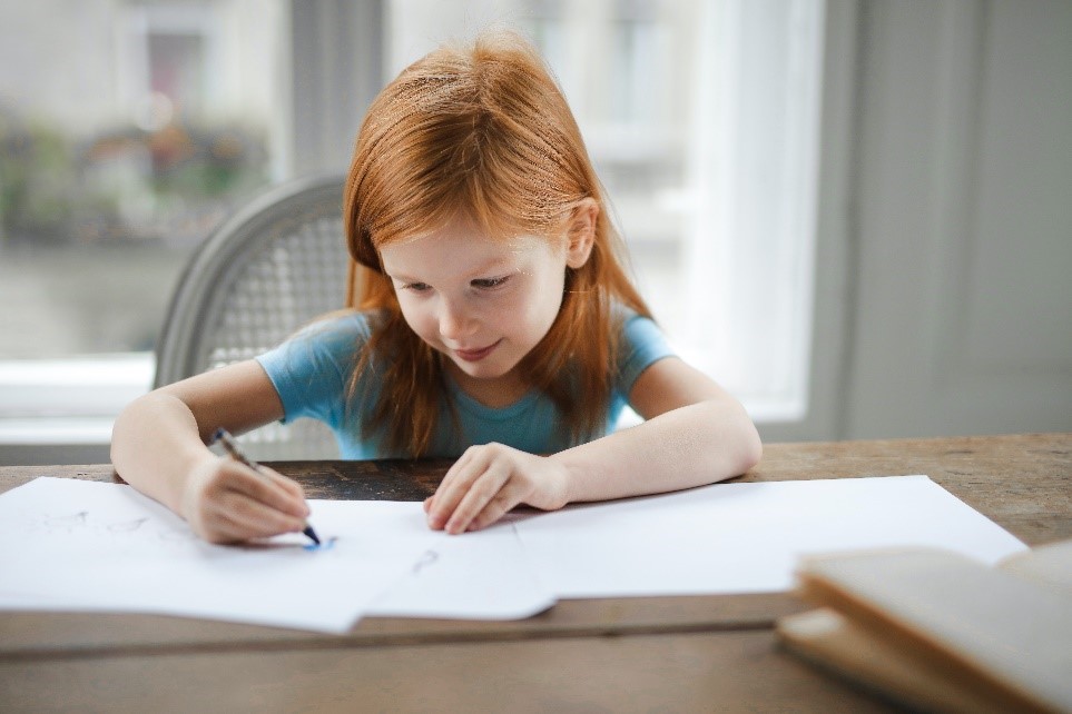 ryšavé dievčatko píše na biely papier za stolom