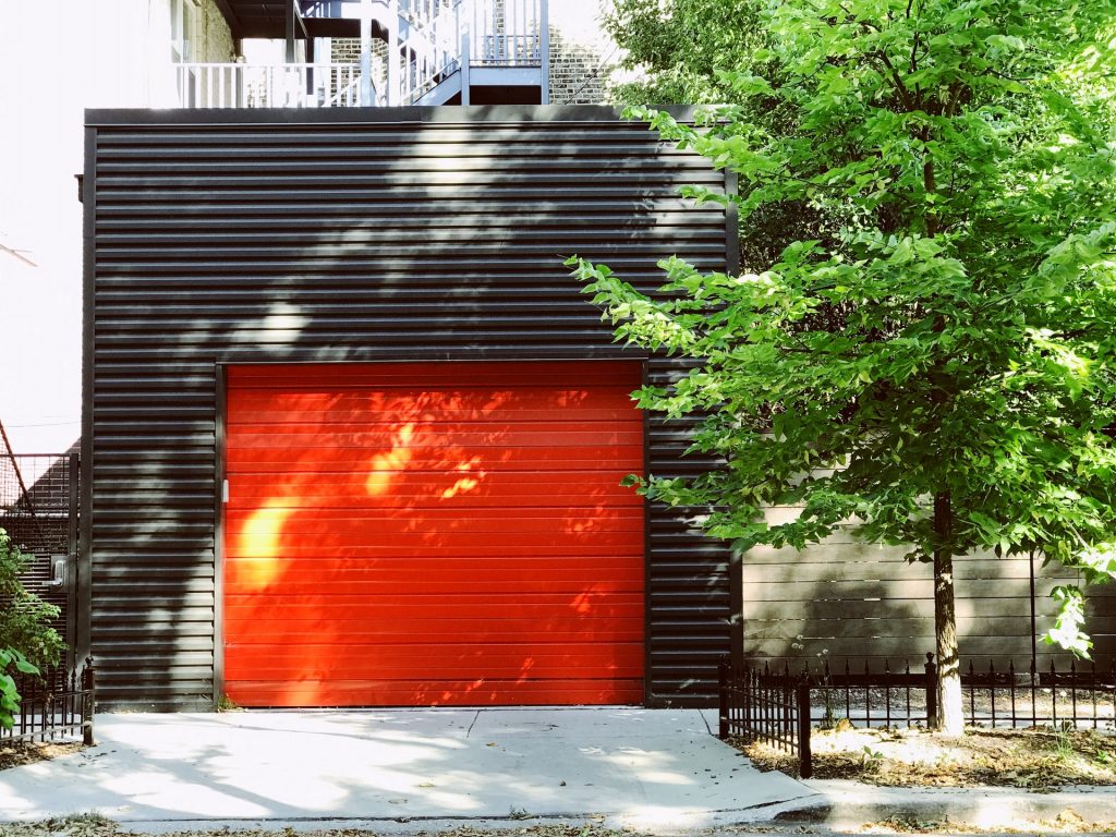 červená garážová brána s malým dvorom a stromom