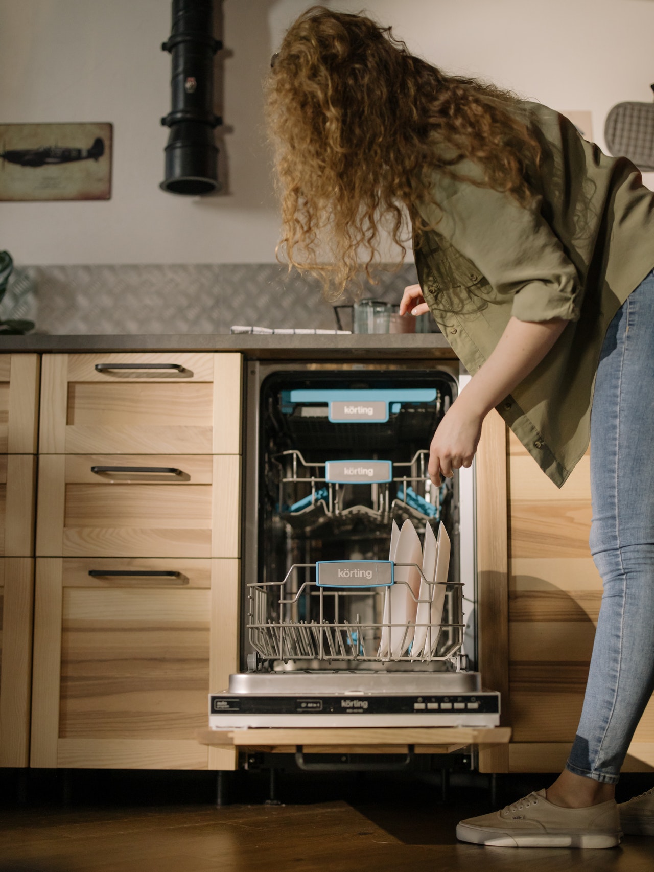 mladá žena stojaca pred čistou umývačkou riadu v smart kuchyni