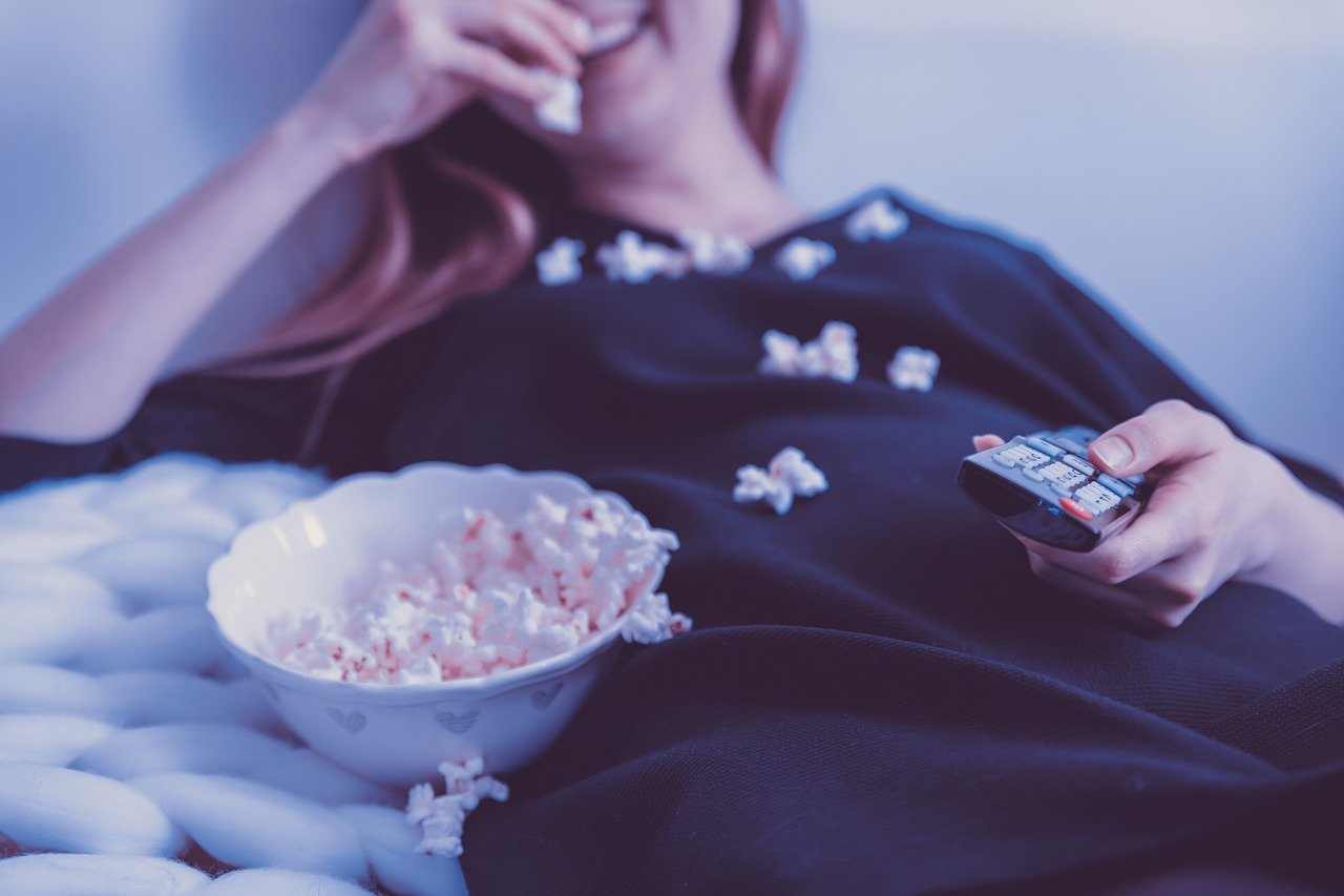mladá žena sleduje dokumentárny seriál IKONY s popcornom