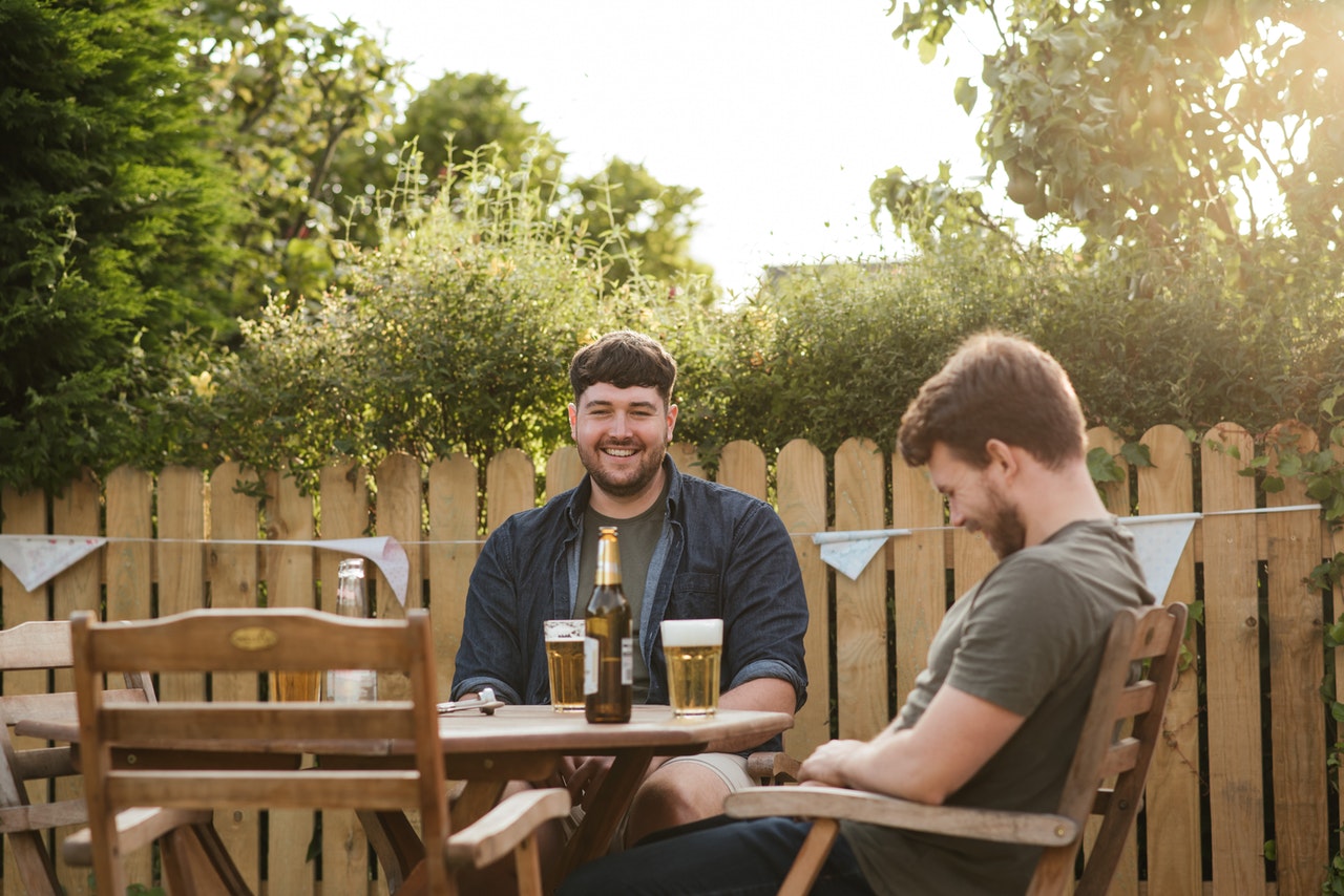 dvaja mladí muži sediaci na terase pri fľaši s pivom