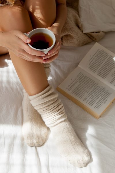 Posteľ žena v ponožkách kniha šálka kávy
